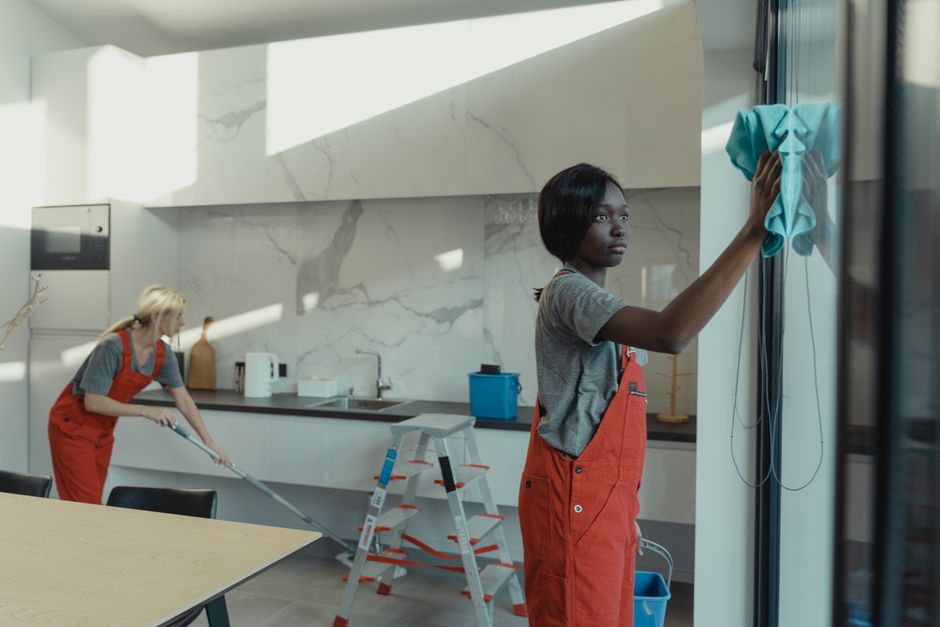 Crop unrecognizable woman in yellow rubber gloves cleaning white tiles with spray and soapy sponge