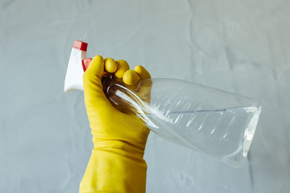 A man using a multi-purpose cleaner and sponge to clean a table indoors, emphasizing hygiene.